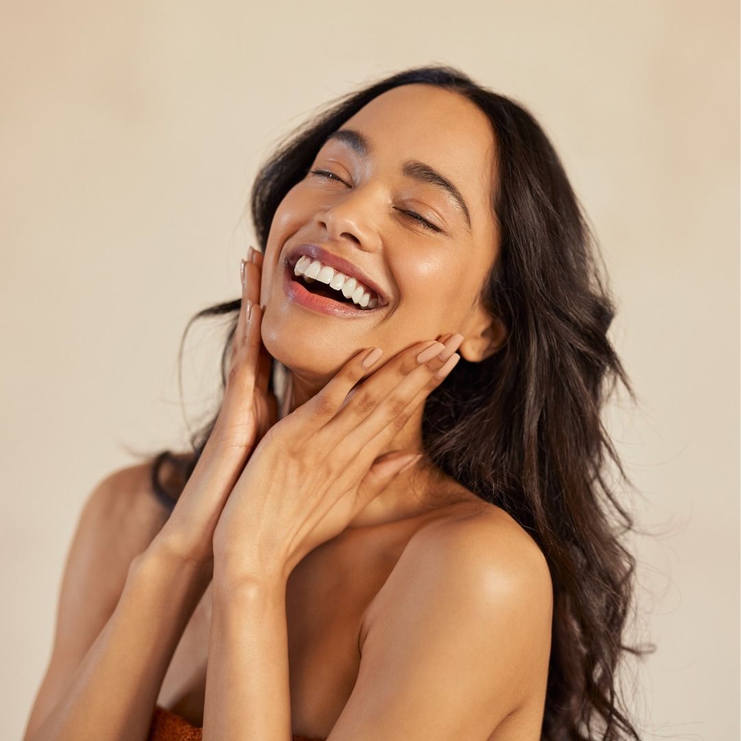 A woman smiling with her hands resting gently on her cheeks