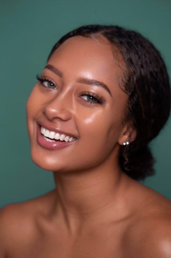 A woman smiling against a muted teal backdrop