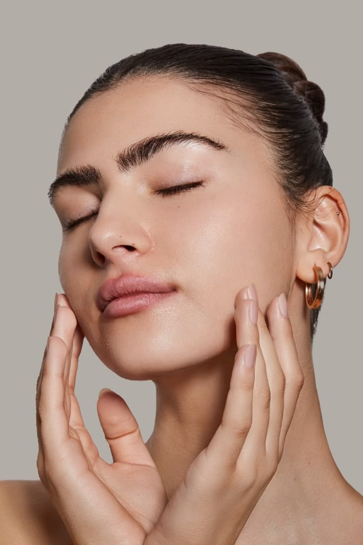 A woman with closed eyes gently touching her face during a skincare ritual